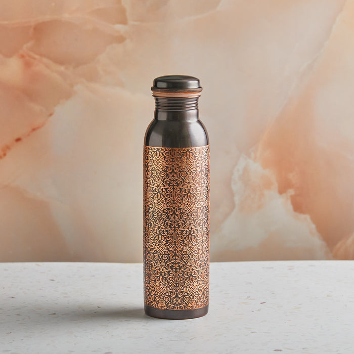 A pure copper ayurvedic water bottle with a black etched design, placed on a marble surface.