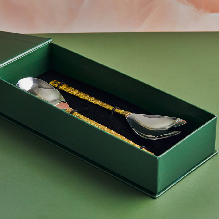 A stainless steel salad server with a brass handle, presented in a green box with a molded interior for each piece.