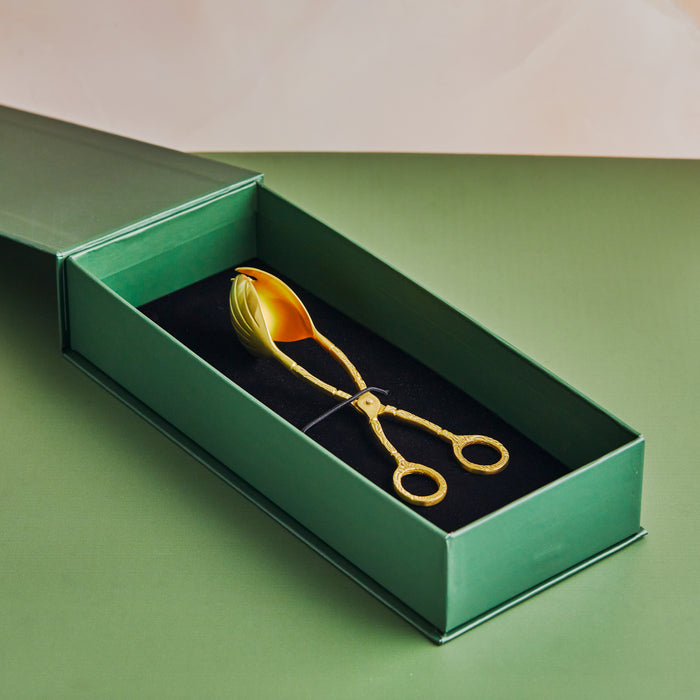 A handcrafted pure brass salad tong with a gold finish, resting inside a green and black box.