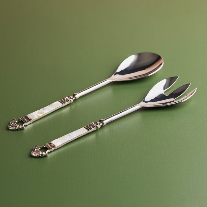 A set of two silver cake servers with mother of pearl handles on a green background.
