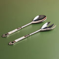 A set of two silver cake servers with mother of pearl handles on a green background.