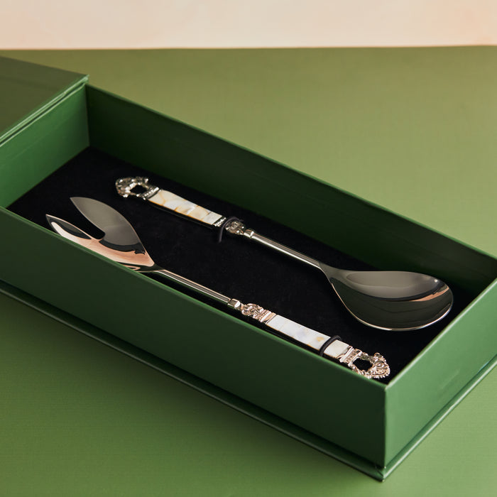 A set of two silver cake servers with mother of pearl handles on a green background.