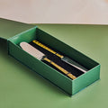 A 2-piece cake knife and server set with brass handles, placed in an open green box on a green background.
